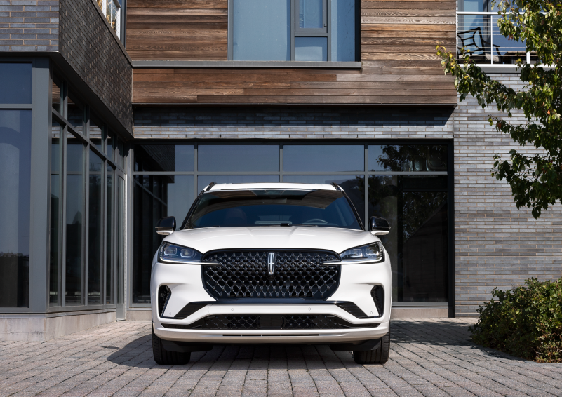 A white 2025 Lincoln Aviator® SUV is shown parked outside a modern building with gray brick and wood accents. | North Park Lincoln in San Antonio TX