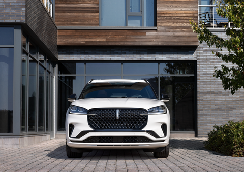 A white 2025 Lincoln Aviator® SUV is shown parked outside a modern building with gray brick and wood accents. | North Park Lincoln in San Antonio TX