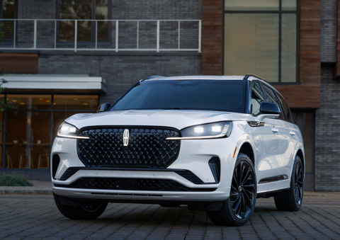 A white 2025 Lincoln Aviator® SUV is shown parked outside a modern building with gray brick and wood accents. | North Park Lincoln in San Antonio TX