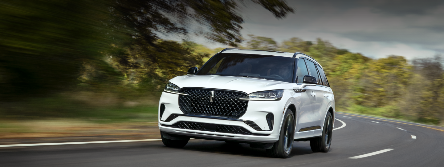 A white 2025 Lincoln Aviator® SUV is being driven down a road lined with trees. | North Park Lincoln in San Antonio TX