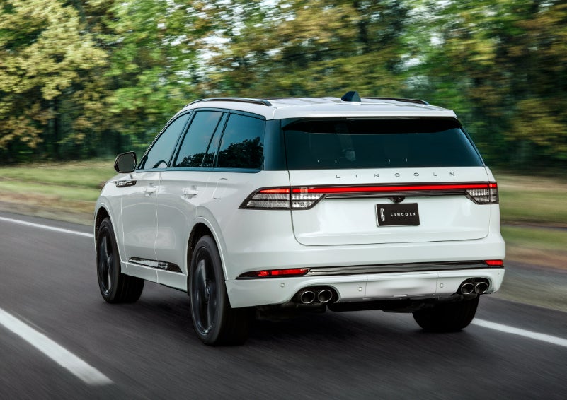 A white 2026 Lincoln Aviator® SUV is being driven away down a road lined with colorful trees. | North Park Lincoln in San Antonio TX
