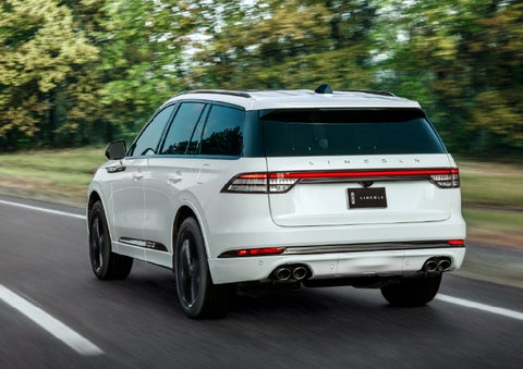 A white 2026 Lincoln Aviator® SUV is being driven away down a road lined with colorful trees. | North Park Lincoln in San Antonio TX